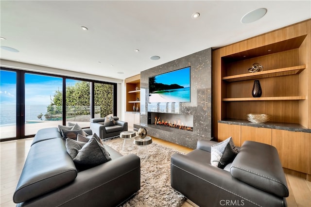 living room featuring built in shelves, light wood-type flooring, a high end fireplace, and a water view