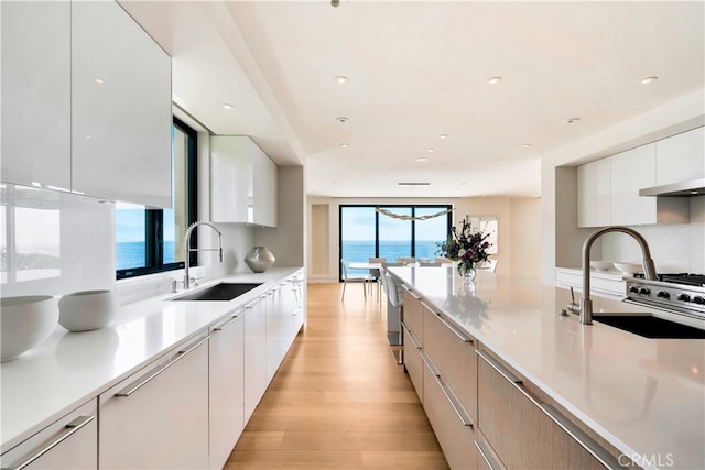 kitchen featuring sink, light hardwood / wood-style flooring, white cabinets, and a water view