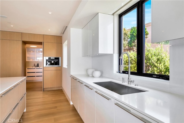 kitchen with light brown cabinets, light wood-type flooring, white cabinetry, stainless steel microwave, and sink