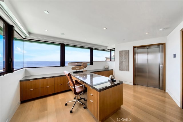 office space with light wood-type flooring, elevator, and a water view