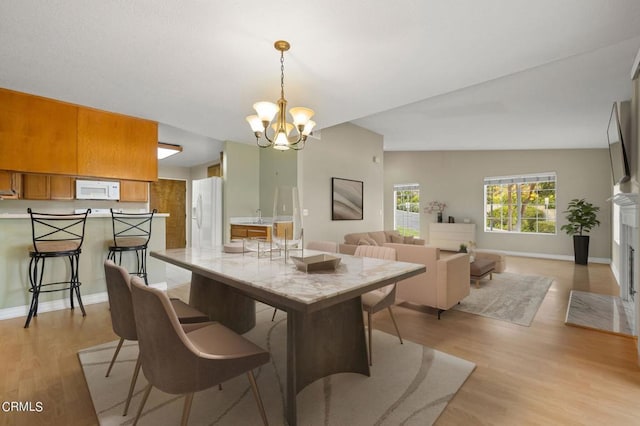 dining area with light hardwood / wood-style flooring, vaulted ceiling, and a notable chandelier