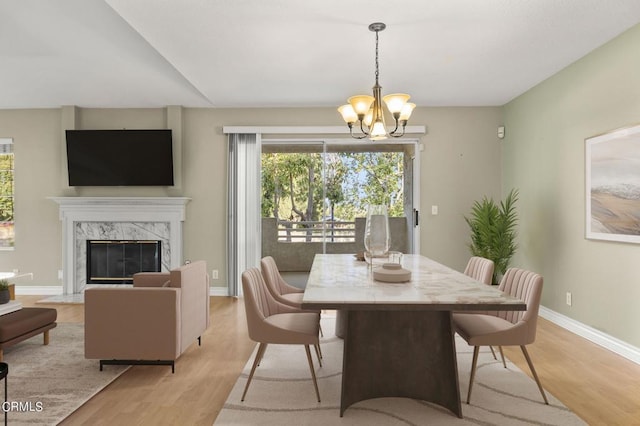 dining space featuring a high end fireplace, light hardwood / wood-style floors, and an inviting chandelier