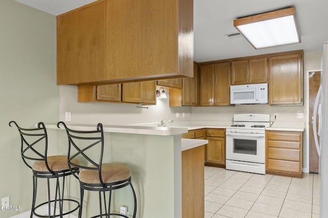 kitchen with a kitchen breakfast bar, kitchen peninsula, light tile patterned floors, and white appliances