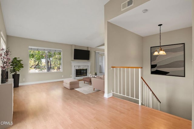 living room featuring a high end fireplace, an inviting chandelier, and light hardwood / wood-style flooring