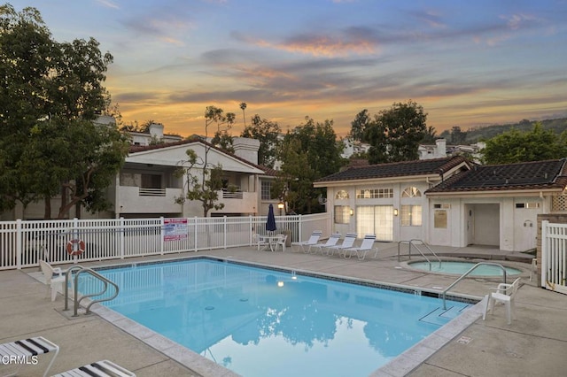 pool at dusk with a patio and a hot tub