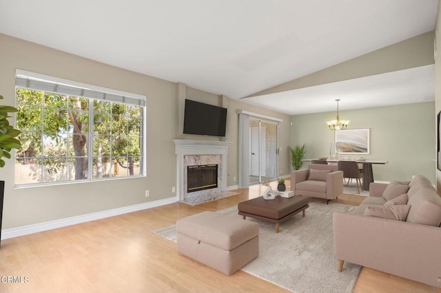 living room featuring light hardwood / wood-style floors, an inviting chandelier, lofted ceiling, and a premium fireplace