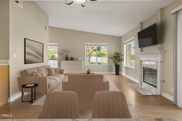 living room featuring a healthy amount of sunlight, vaulted ceiling, a fireplace, and light hardwood / wood-style flooring