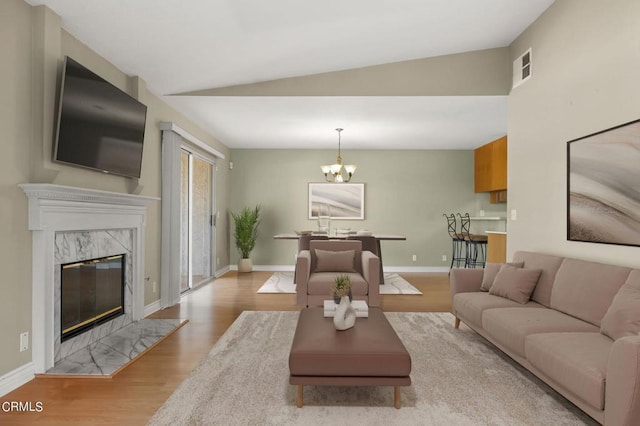 living room with vaulted ceiling, an inviting chandelier, light hardwood / wood-style flooring, and a premium fireplace