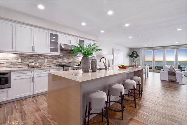 kitchen with a breakfast bar, a kitchen island with sink, white cabinets, oven, and sink