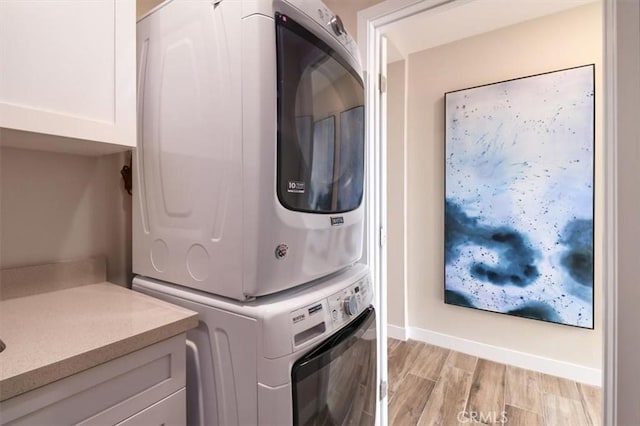 laundry room with cabinets, stacked washer and dryer, and light hardwood / wood-style floors