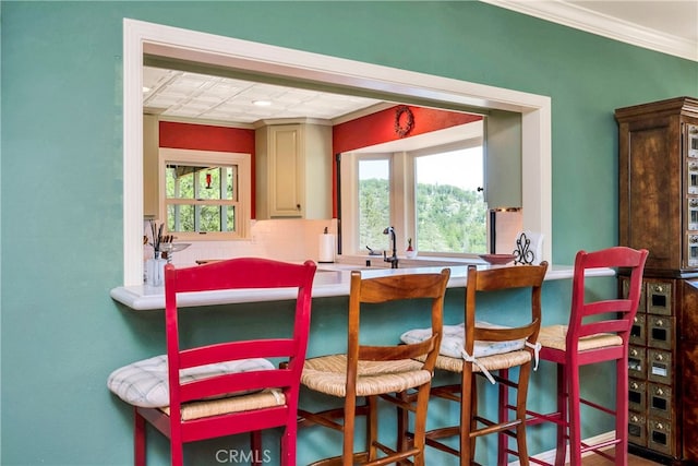 kitchen with ornamental molding, a healthy amount of sunlight, backsplash, and cream cabinets