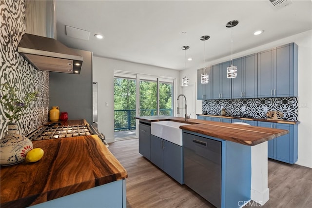 kitchen featuring dishwasher, wooden counters, wall chimney range hood, sink, and blue cabinetry