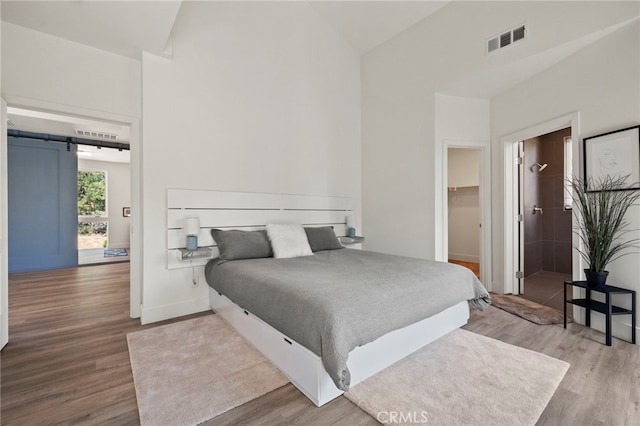 bedroom with hardwood / wood-style floors, a walk in closet, a barn door, and lofted ceiling