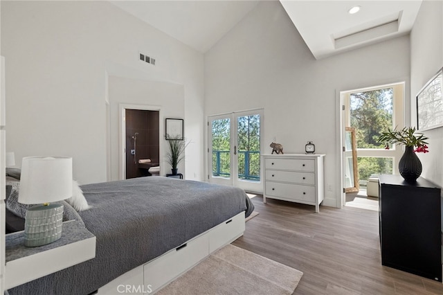 bedroom with wood-type flooring, ensuite bathroom, high vaulted ceiling, and multiple windows