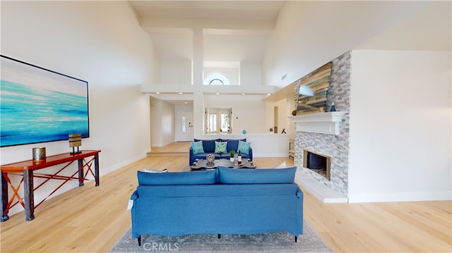 living room with hardwood / wood-style flooring, a towering ceiling, and a stone fireplace