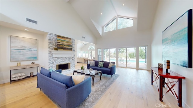 living room featuring a stone fireplace, light hardwood / wood-style flooring, and a high ceiling