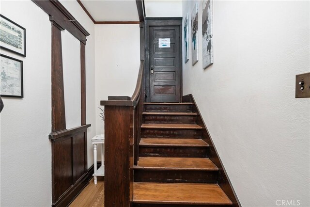 stairs with wood-type flooring and ornamental molding