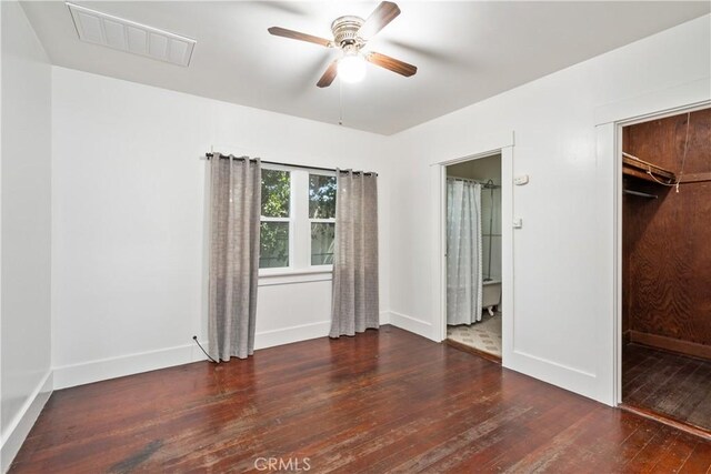 unfurnished bedroom featuring ensuite bath, ceiling fan, dark wood-type flooring, a walk in closet, and a closet