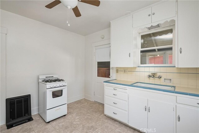 kitchen with white cabinets, sink, ceiling fan, white gas range, and tasteful backsplash