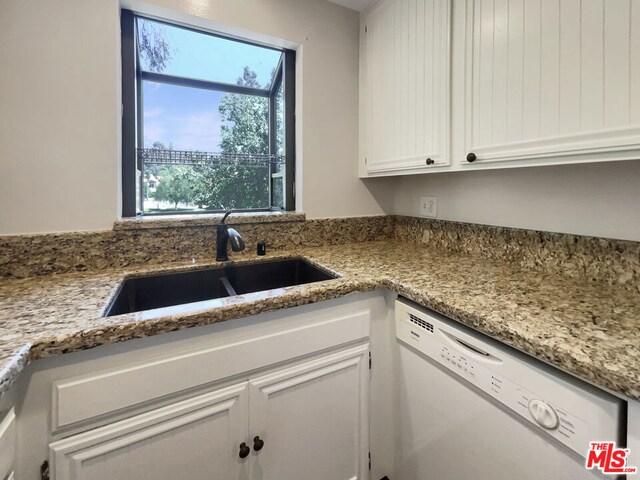 kitchen featuring stainless steel dishwasher, light stone counters, white cabinets, and sink