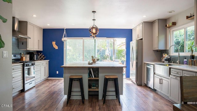 kitchen with appliances with stainless steel finishes, a center island, a healthy amount of sunlight, and wall chimney range hood