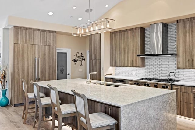 kitchen featuring pendant lighting, backsplash, a kitchen island with sink, and wall chimney exhaust hood