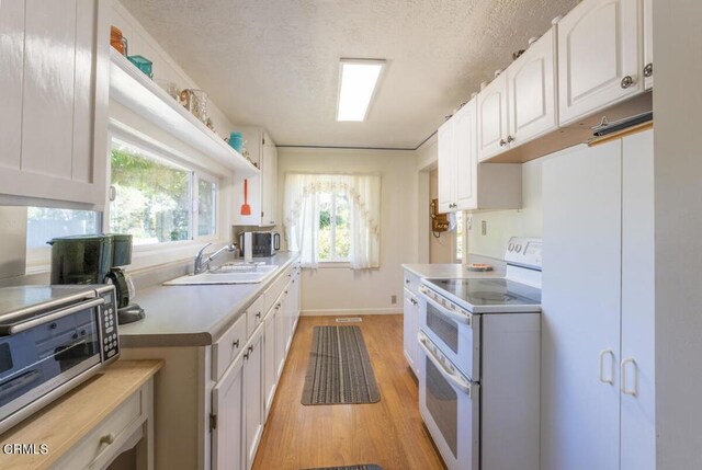 kitchen with sink, range with two ovens, light hardwood / wood-style flooring, and white cabinets