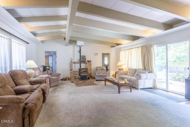 carpeted living room with vaulted ceiling with beams and a wood stove