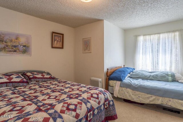 bedroom featuring carpet flooring, a textured ceiling, and radiator heating unit