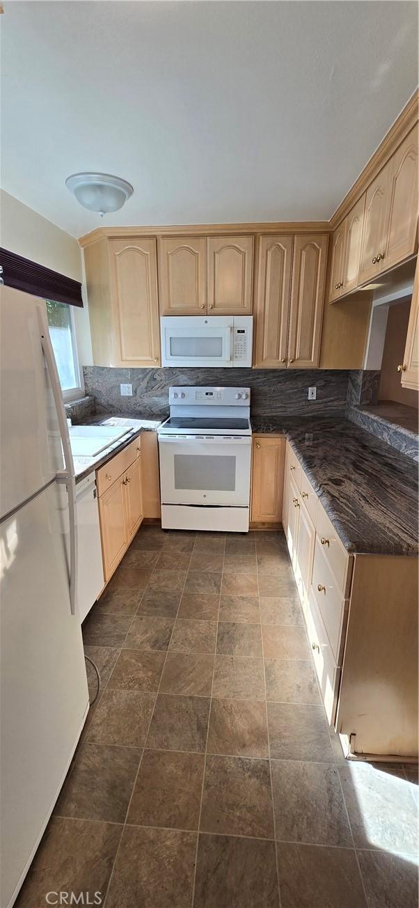 kitchen with light brown cabinets, white appliances, backsplash, and dark stone counters