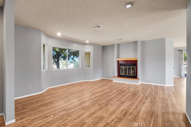 unfurnished living room with a textured ceiling, light wood-type flooring, and a healthy amount of sunlight