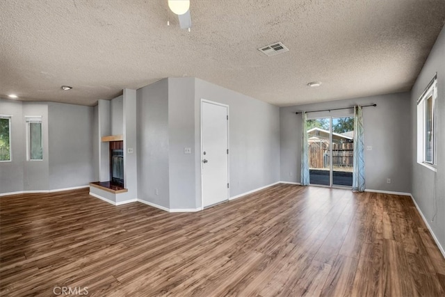 unfurnished living room with a textured ceiling, wood-type flooring, a multi sided fireplace, and ceiling fan