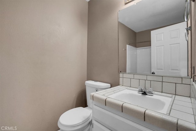 bathroom featuring walk in shower, vanity, toilet, and tasteful backsplash