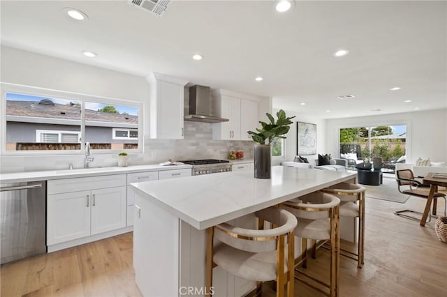 kitchen featuring white cabinetry, wall chimney exhaust hood, stainless steel appliances, light hardwood / wood-style floors, and a breakfast bar area