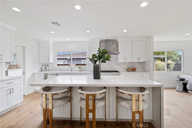 kitchen with a kitchen bar, light wood-type flooring, and wall chimney range hood