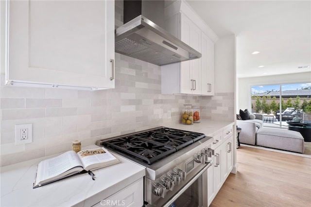 kitchen with wall chimney exhaust hood, stainless steel range, tasteful backsplash, light hardwood / wood-style floors, and light stone counters