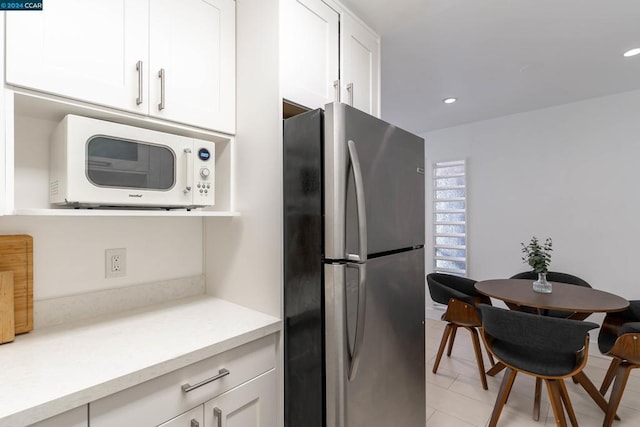 kitchen featuring stainless steel fridge, white cabinetry, and light tile patterned floors