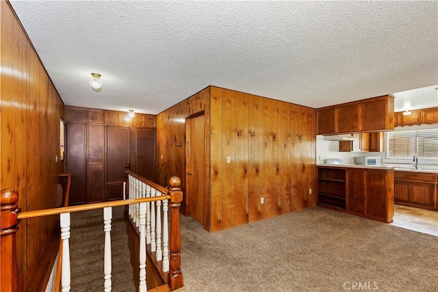 hall with light carpet, a textured ceiling, and wood walls