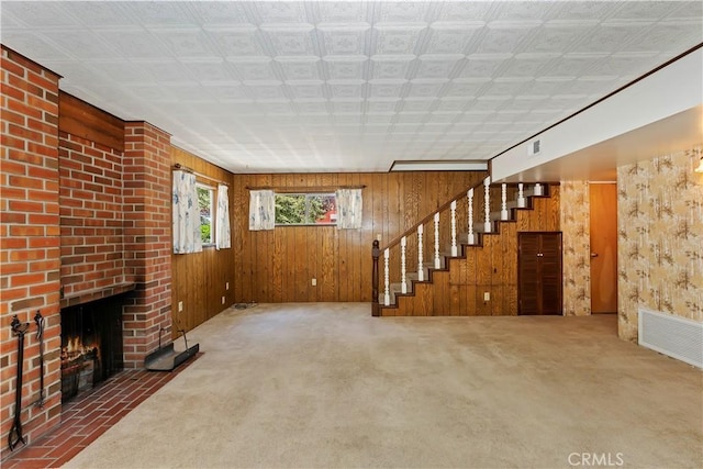 unfurnished living room with a brick fireplace, wood walls, and carpet