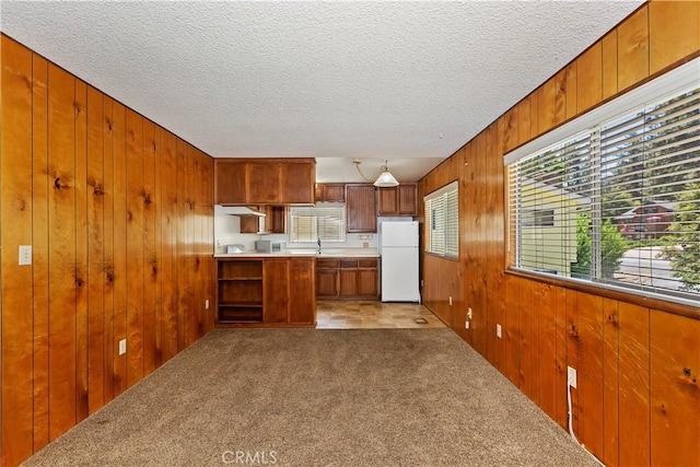 kitchen featuring a textured ceiling, decorative light fixtures, white refrigerator, wood walls, and light colored carpet