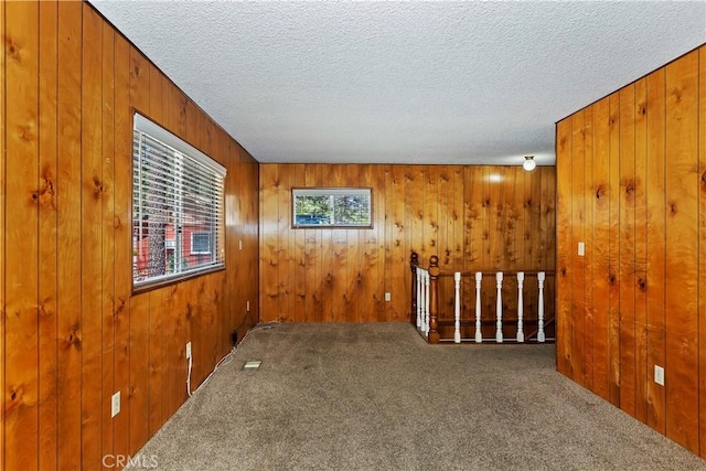 carpeted empty room featuring a textured ceiling and wooden walls