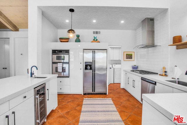 kitchen with washer and clothes dryer, stainless steel appliances, wine cooler, wall chimney range hood, and pendant lighting