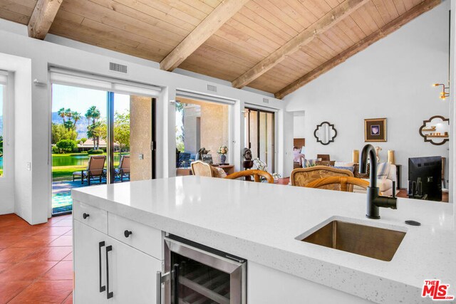 kitchen with white cabinets, beverage cooler, wood ceiling, sink, and lofted ceiling with beams