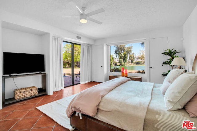 tiled bedroom featuring a textured ceiling, ceiling fan, a water view, and access to outside