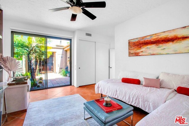 bedroom with a textured ceiling, a closet, access to outside, ceiling fan, and light tile patterned floors