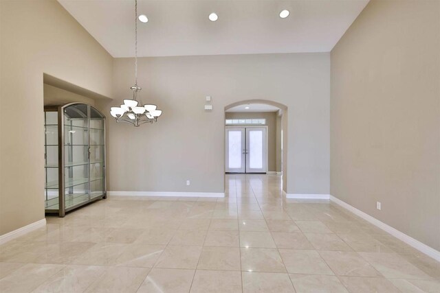 tiled empty room with french doors, lofted ceiling, and a chandelier