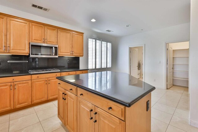 kitchen with appliances with stainless steel finishes, light tile patterned floors, decorative backsplash, and a center island