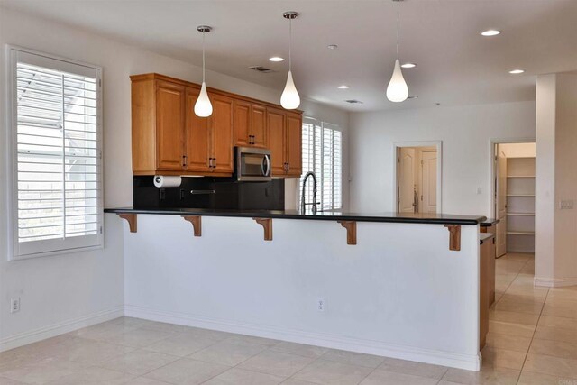 kitchen with pendant lighting, a wealth of natural light, kitchen peninsula, and a kitchen bar