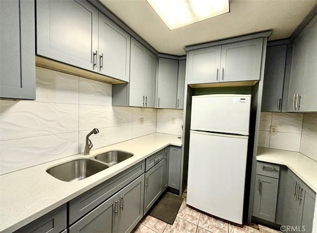 kitchen with gray cabinets, light tile patterned flooring, tasteful backsplash, sink, and white refrigerator