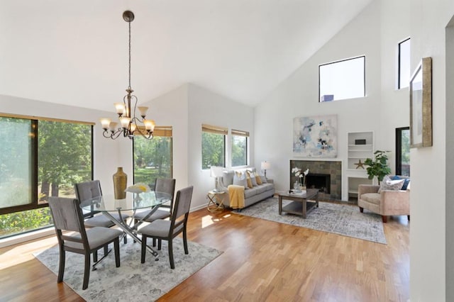 dining area with a chandelier, a fireplace, wood-type flooring, and high vaulted ceiling